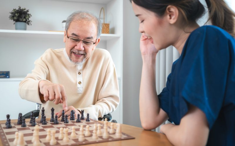 Senior man playing chess with woman at home, smiling game